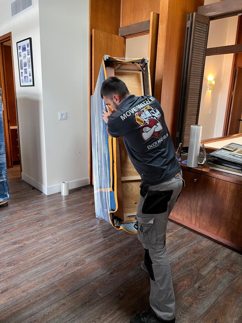 Mover carefully carrying a padded cabinet frame through a home