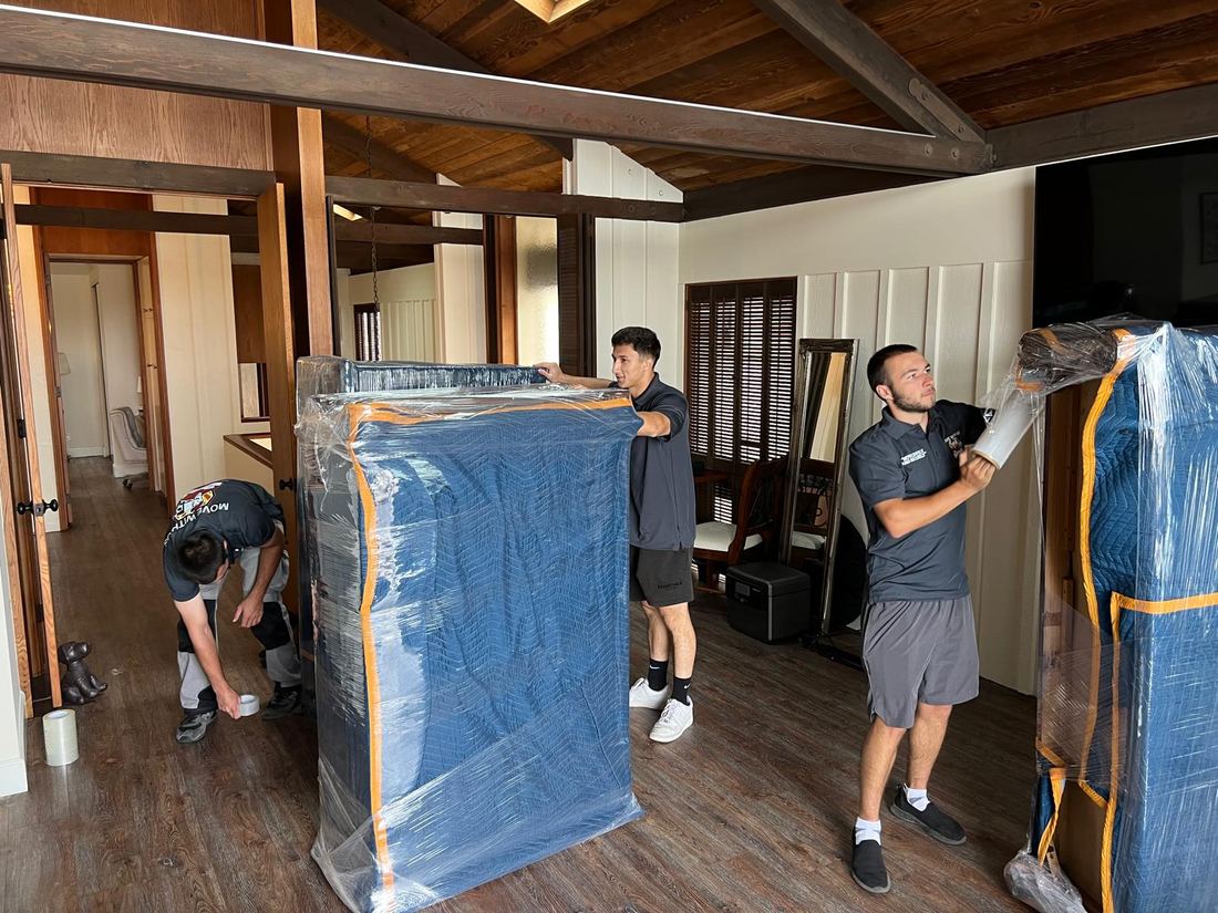 Four All Way Moving crew members padding and stretch-wrapping furniture inside a Long Beach home