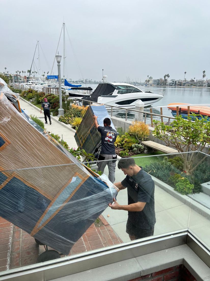 Movers carrying wrapped furniture along the Naples canal walkway in Long Beach